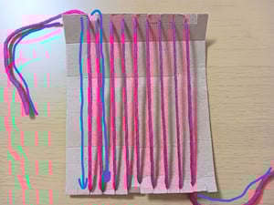 切り込みが入った段ボールに縦にピンクの毛糸をかけた写真