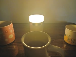 小さなライトをおいた机にマグカップが3つ並べられた写真